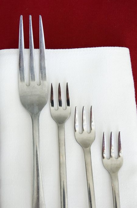 Large dinner fork and three smaller forks on red and white linen