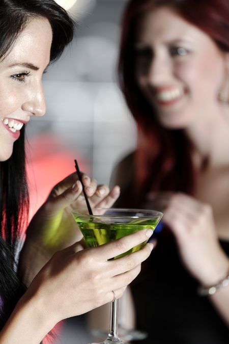 Two beautiful young woman chatting and drinking cocktails at a nightclub or wine bar.