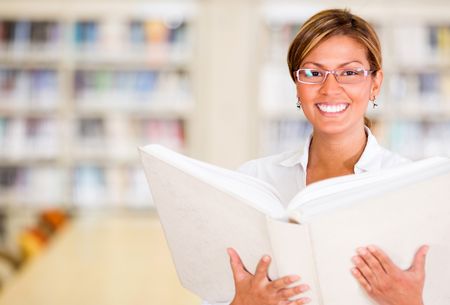 Happy librarian holding a book and smiling at the library