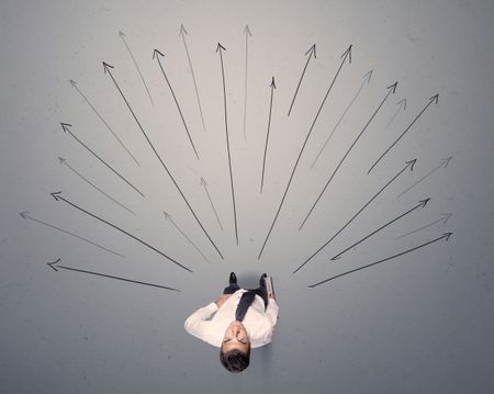 Young contemplating businessman stands in front of grey arrows 