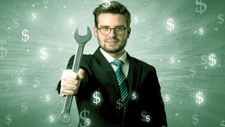 Handsome businessman holding tool with dollar symbols around and with green background