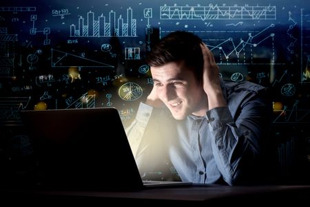 Young handsome businessman working late at night in the office with blue calculations in the background