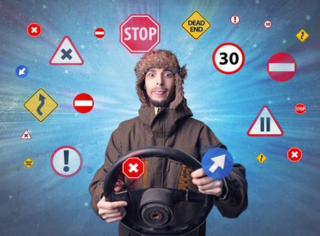 Young man holding black steering wheel with road signs surrounding him