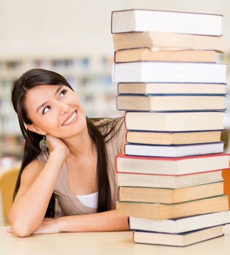 Female student with a pile of books at the library