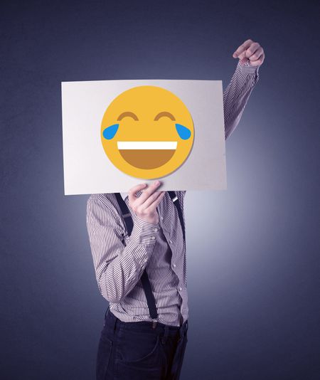 Young businessman hiding behind a laughing emoticon on cardboard