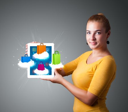 beautiful woman holding modern tablet with colorful shopping bags on clouds