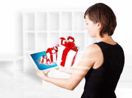 Young woman looking at modern tablet with present boxes