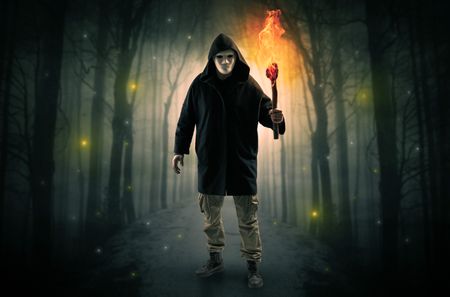 Mysterious man coming from a path in the forest with burning flambeau concept