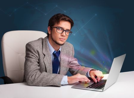 Handsome young man sitting at desk and typing on laptop with abstract lights