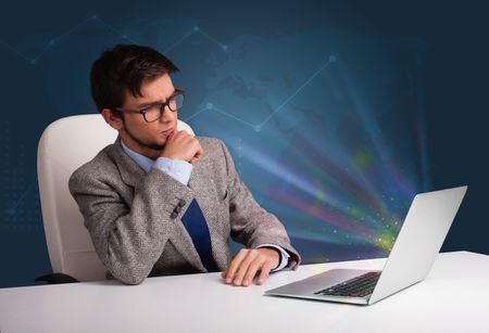 Handsome young man sitting at desk and typing on laptop with abstract lights