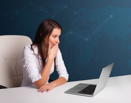 Pretty young woman sitting at desk and typing on laptop