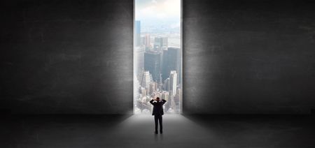 Businessman standing in a dark room and looking outside to a cityscape view