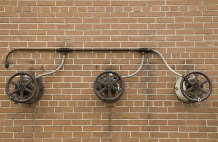 Iron wheels of three locked water valves connected to the same pipe on exterior red brick wall