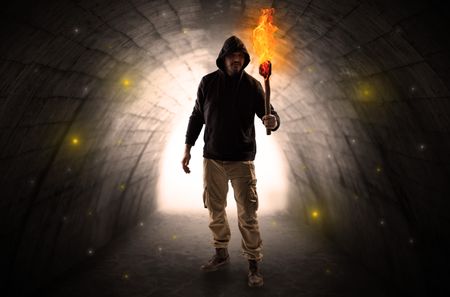 Ugly man with burning flambeau walking in a dark tunnel