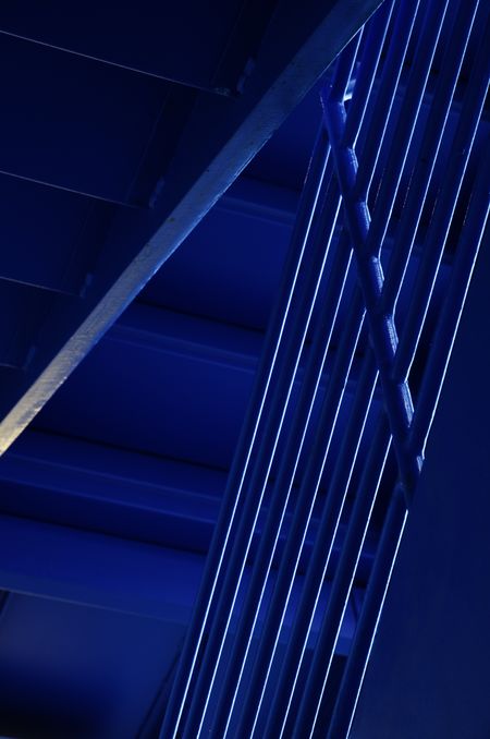 Handrails and undersides of stairs in stairwell lit by daylight from blue windows of a city parking garage