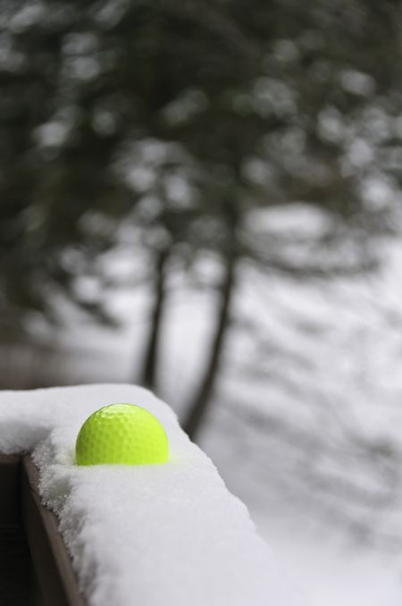 Yellow golf ball in snow on ledge in winter (selective focus)