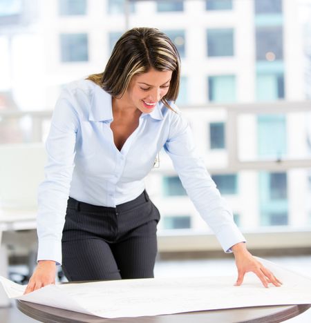 Female architect looking at blueprints at the office
