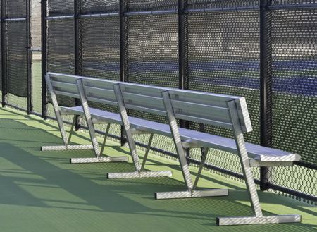 Vacant aluminum bench behind fence around tennis court on campus of community college