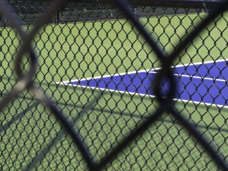 Vision of privilege: Corner of tennis court seen through two wire mesh fences (selective focus)