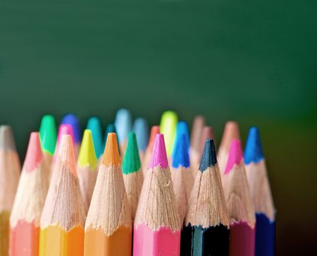 assorted colour pencils in vibrant tones in front of a blackboard in a classroom