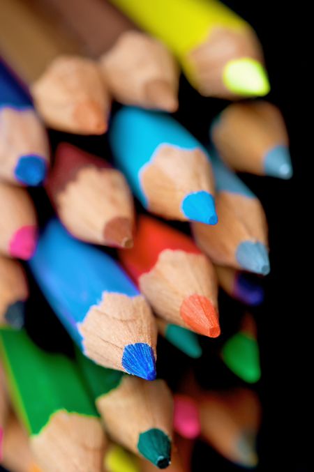 assorted colour pencils close up in perspective with focus on the tips using a shallow depth of field - isolated over a black background