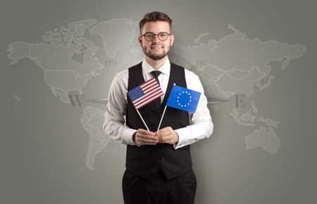 Cheerful businessman standing in front of a map with flag on his hand