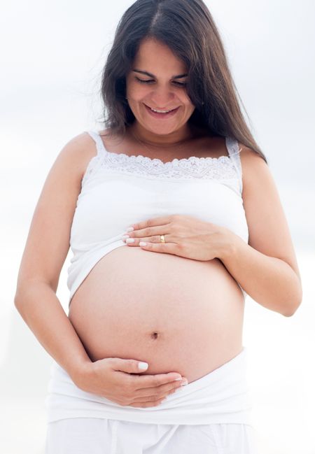 Pregnant woman stroking her belly and smiling outdoors