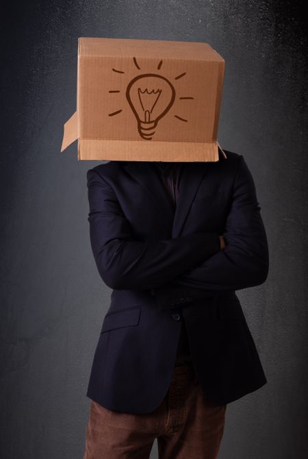 Young man standing and gesturing with a cardboard box on his head with light bulb