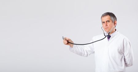 Middle aged doctor listening to empty copy space with stethoscope