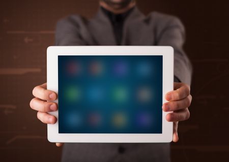 Young businessman holding a white modern tablet with blurry apps