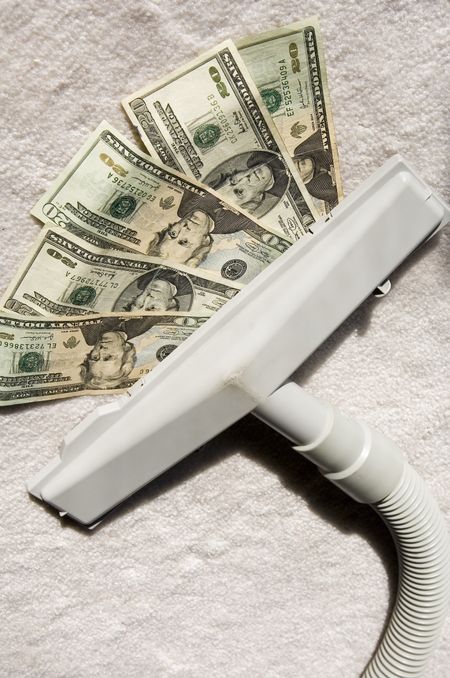 Attachment to vacuum cleaner sucking up five $20 bills on sunlit white carpet