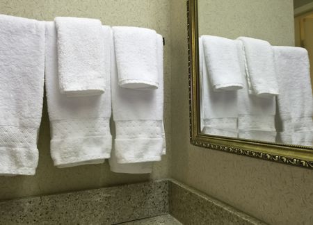 Housekeeping at a glance: Five white terrycloth towels reflected by wall mirror in hotel bathroom
