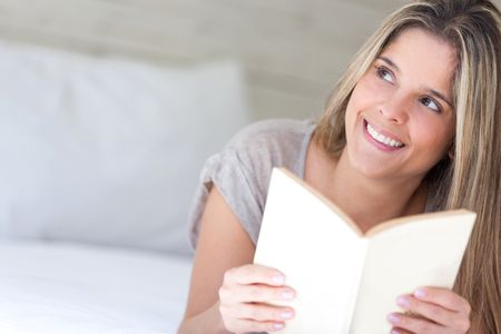 Thoughtful woman reading a book at home and smiling