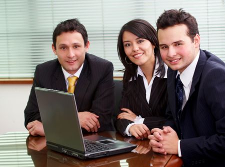 businessmen and businesswomen in a business meeting in an office smiling with a laptop on the table