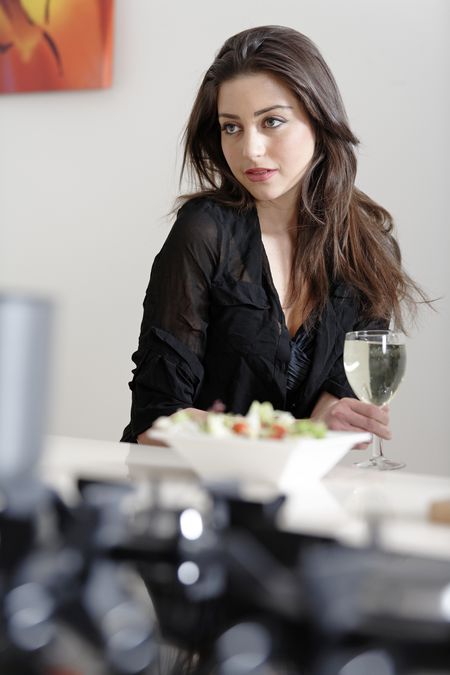 Beautiful young woman enjoying a glass of wine in her kitchen, while preparing food.