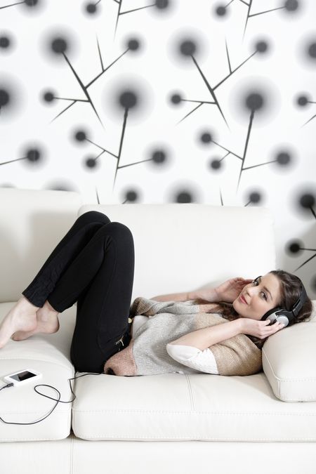 Attractive woman sat on a white sofa listening to music