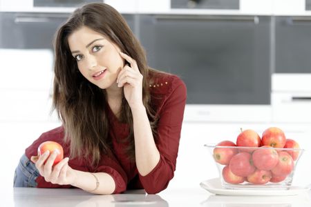 Beautiful young woman eating an apple in her white kitchen