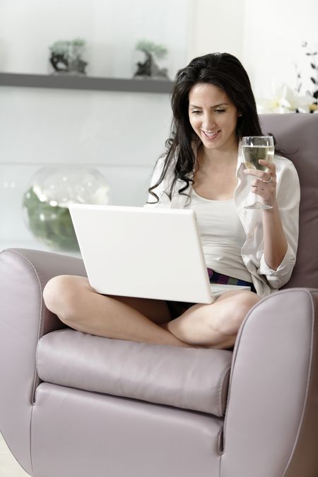 Beautiful young woman enjoying a glass of wine in her elegant living room.