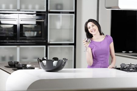 Attractive young woman in a dinner dress holding a glass of wine in her kitchen.