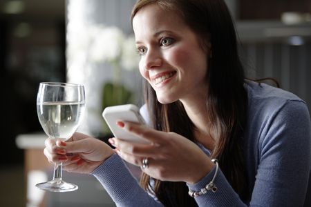 Attractive young woman enjoying a glass of wine in her kitchen while chatting on the phone.