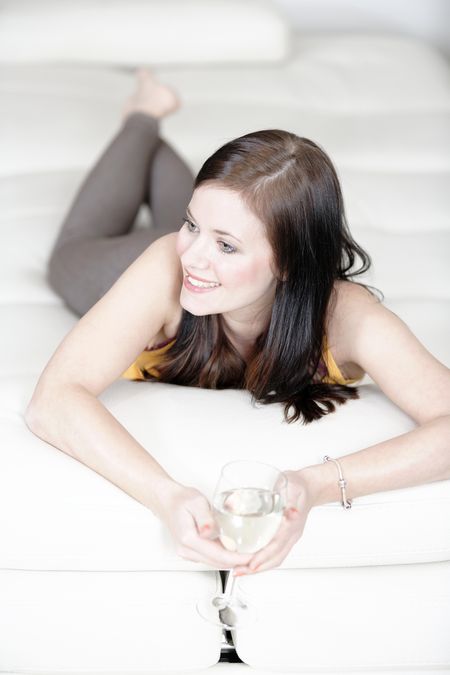 Attractive young woman lying on her sofa enjoying a glass of wine.