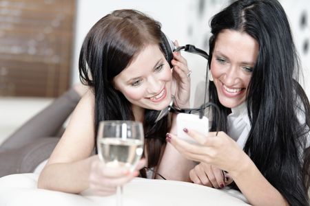Two beautiful young woman listening to music on headphones at home on the sofa.