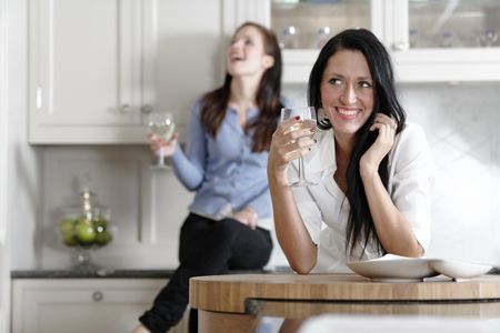 Two attractive young friends laughing and drinking wine in their kitchen.