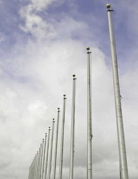 Legacy of winter: Row of flagpoles without flags against a partly cloudy sky in spring, northern Illinois