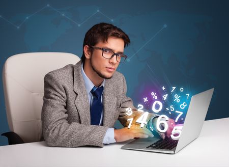 Handsome young man sitting at desk and typing on laptop with 3d numbers comming out