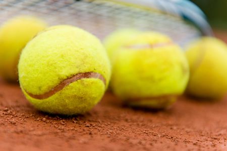 Tennis balls at the clay court with a racket