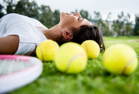Female tennis player lying outdoors daydreaming with victory