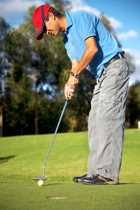male golfer in putting green about to put the ball in the hole - focus is on the ball