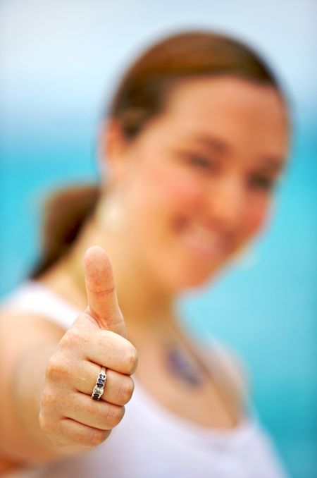 casual girl doing the thumbs up sign with the sea in the background