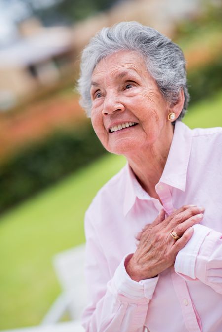 Sweet elder woman with hands on chest looking happy - outdoors